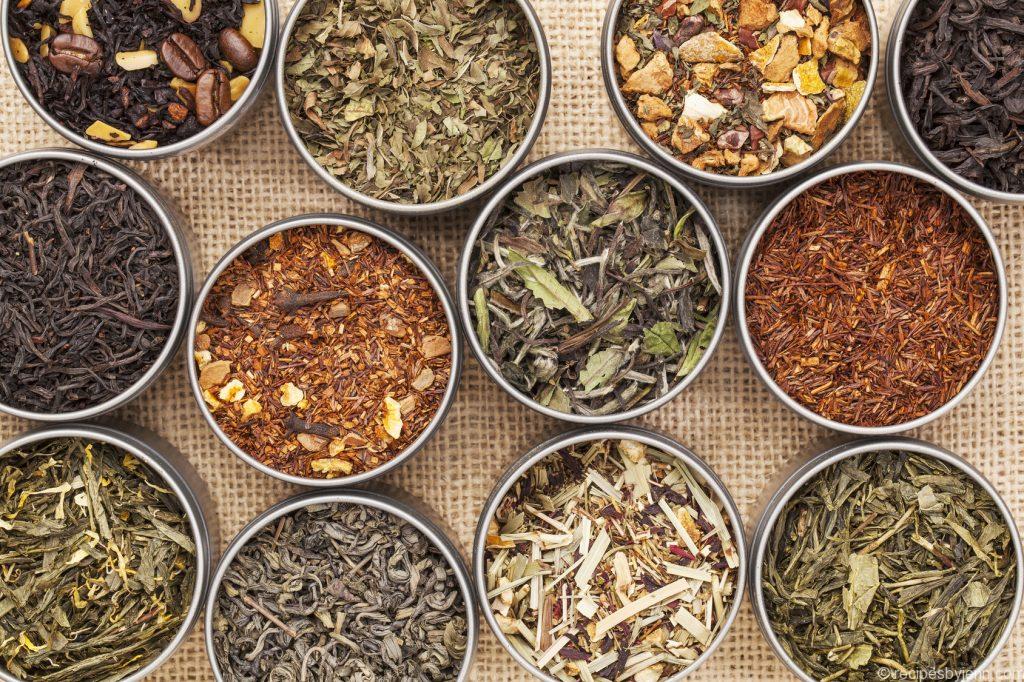 samples of loose leaf green, white, black and herbal tea in metal cans on canvas background